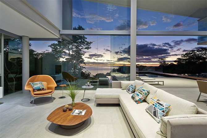 Вітальня з каміном Вітальня в скляному будинку з каміном та видом на океан, сучасний дизайн 2026