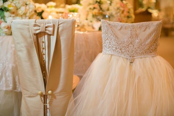 Весільний декор стільців Елегантний декор стільців тканиною та квітами для святкової атмосфери на весіллі.